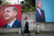 Eine Person läuft an zwei Wahlplakaten vorbei, das eine Plakat zeigt das Porträt von Recep Tayyip Erdoğan, das andere das Porträt von Kemal Kılıçdaroğlu