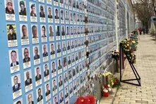 Wand der Erinnerung, St. Michaelskloster, Kyjiw Foto: Eine Gedenkwand mit zahlreichen Porträtfotos verstorbener Soldat*innen. Davor stehen Blumen und Kränze. Ein Gehweg führt entlang der Wand.