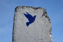 Peace dove on a section of the wall A concrete slab with a blue dove painted on it, broken at the top with exposed metal, set against a blue sky.