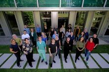 Team Studienwerk Gruppe von etwa 30 Personen steht draußen vor einem Gebäude auf Steinplatten in Gras, frontal zur Kamera blickend.