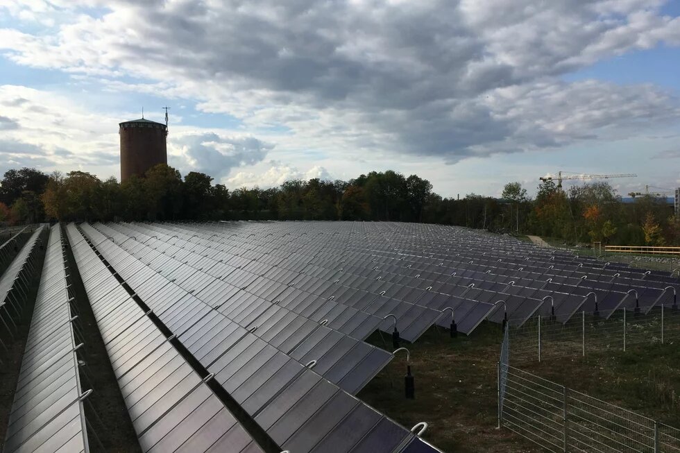 Großflächige Solarthermieanlage Großflächige Solarthermieanlage mit Reihen geneigter Kollektoren, im Hintergrund Bäume, ein Turm und Baukräne.