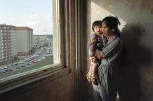 Vietnamesische Vertragsarbeiterin mit Kind am Fenster der Plattenbauwohnung stehend