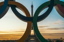 Durch die eine Skulptur der Olympischen Ringe sieht man den Eiffelturm und die Skyline von Paris im Sonnenuntergang.