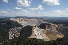 Photo: Mining area near Majdanpek, Serbia, in a hilly landscape. In the foreground is a town with many buildings. On the right, a large open-pit mine with a water basin.
