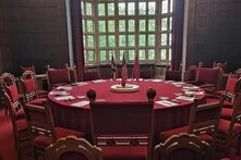 Photo: Conference room in Cecilienhof with a round table, red-upholstered chairs, and large windows in the background. British, American, and Soviet flags in the center of the table.