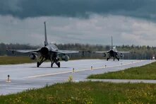 Portuguese Air Force Zwei Kampfjets rollen hintereinander auf nasser Landebahn, Wiese und Wald rechts und links, dunkle Wolken am Himmel.