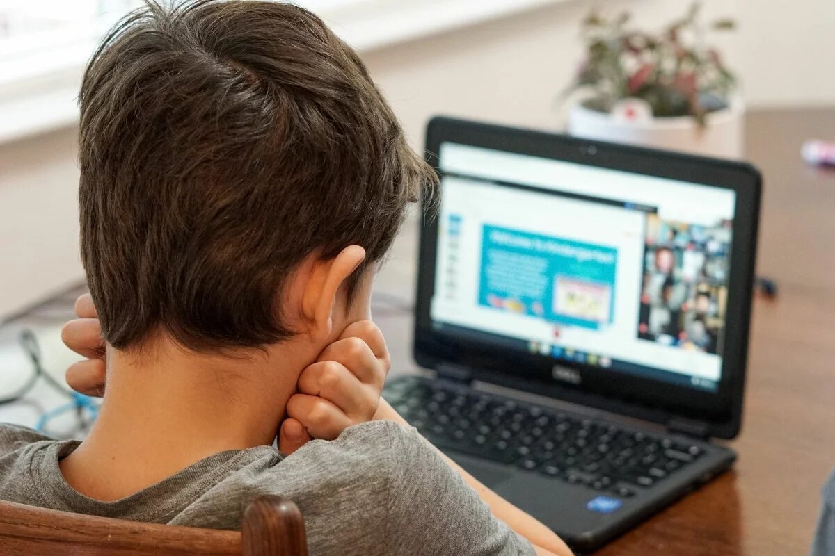 Ein Kind sitzt mit auf den Händen aufgestütztem Kopf vor einem aufgeklappten Laptop