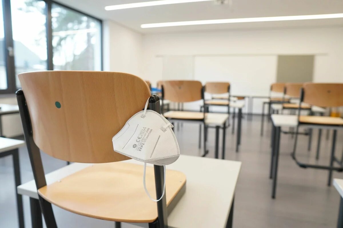 Eine FFP2-Maske hängt an einem Stuhl in einem leeren Klassenzimmer