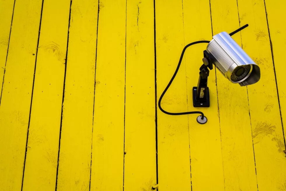Yellow Watcher - Kamera an gelber Bretterwand