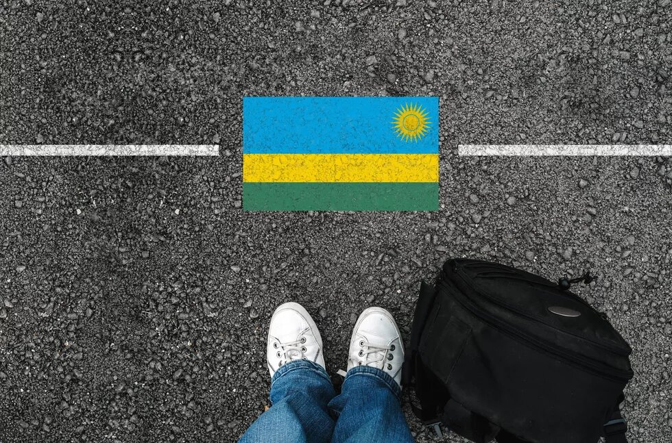 Füße vor eine symbolischen Grenzlinie mit der Flagge des afrikanischen Lands Ruanda