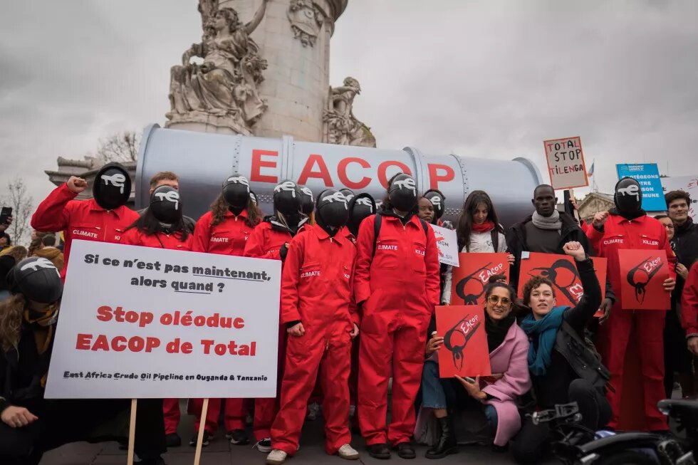Eine Delegation ugandischer Aktivisten schließt sich dem STOP EACOP-Block beim Look UP-Klimamarsch in Paris, Frankreich, an, um das klimaschädliche Projekt von Total, die East Africa Crude Oil Pipeline, anzuprangern. Aktivisten in roten Squid-Game-Kostümen mit Total-Energies-Logo auf Masken halten eine gefälschte Pipeline, um Total aufzufordern, sich von fossilen Brennstoffen zu trennen.