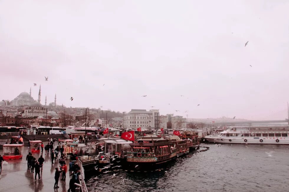 Blick auf den Hafen von Istanbul, an einem Schiff wehen viele türkische Flaggen, darüber ein grauer, regnerischer Himmel