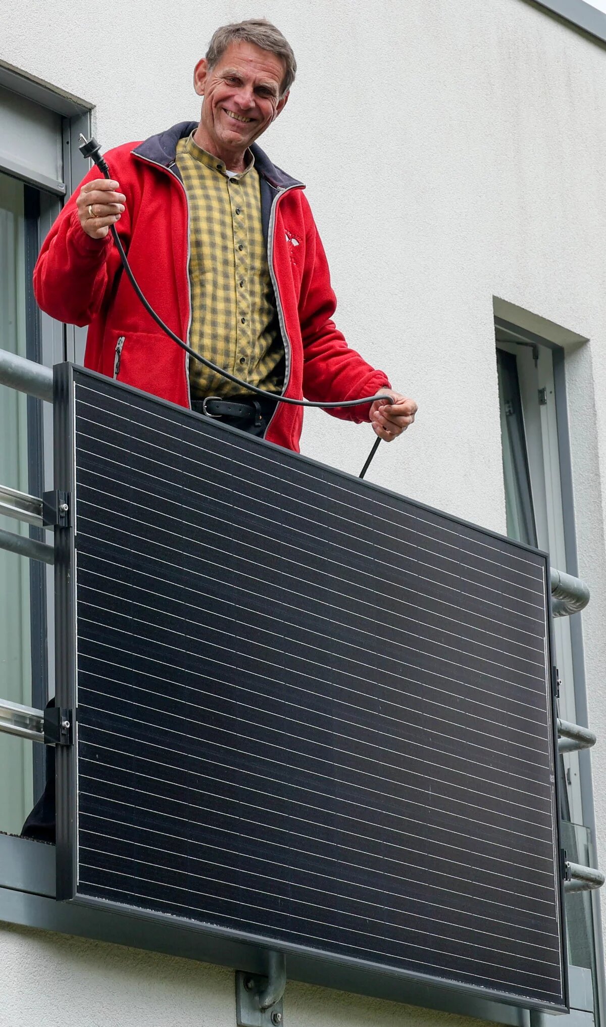 Ein Mensch steht auf einem Balkon und installiert ein Solarpanel