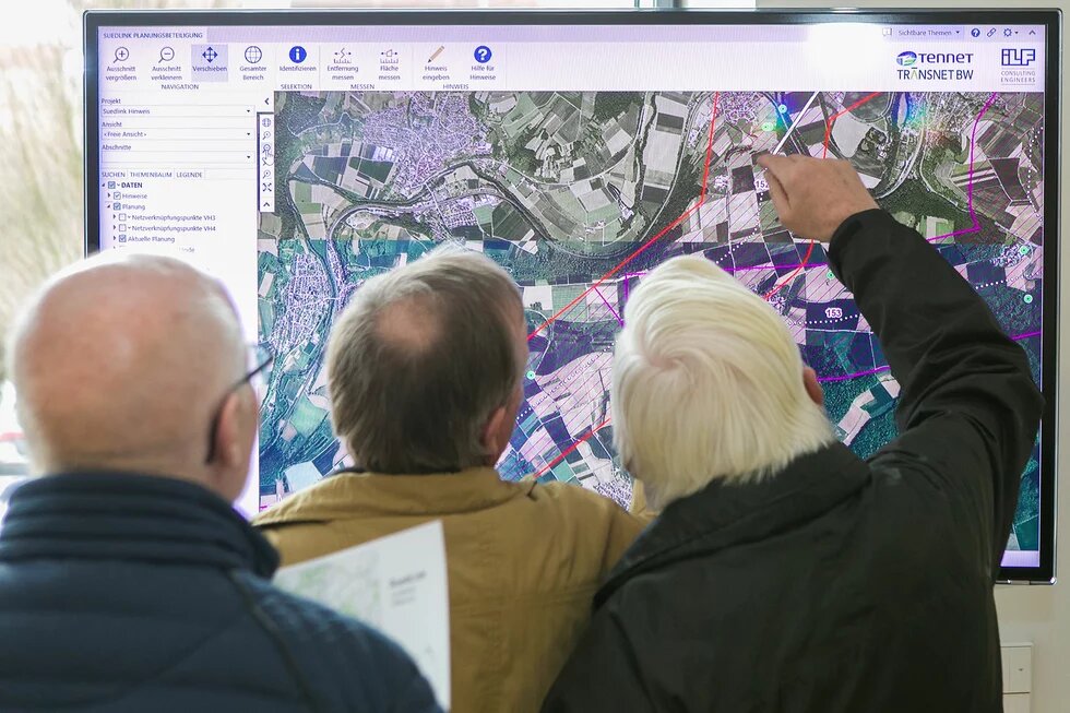 Drei Menschen stehen vor einem großen Bildschirm, auf dem das digitale Planungstool von SuedLink zu sehen ist