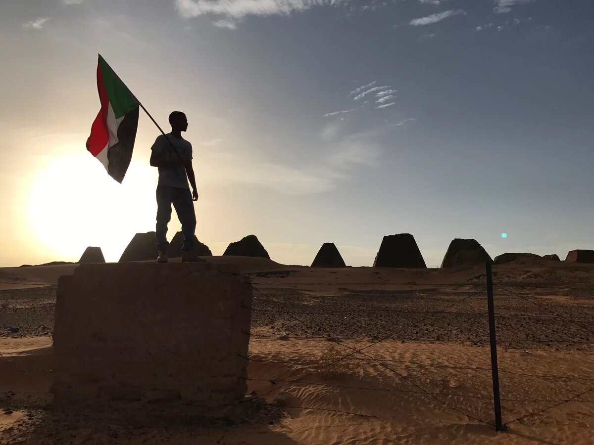 Mensch steht mit Sudanflagge beim Sonnenuntergang