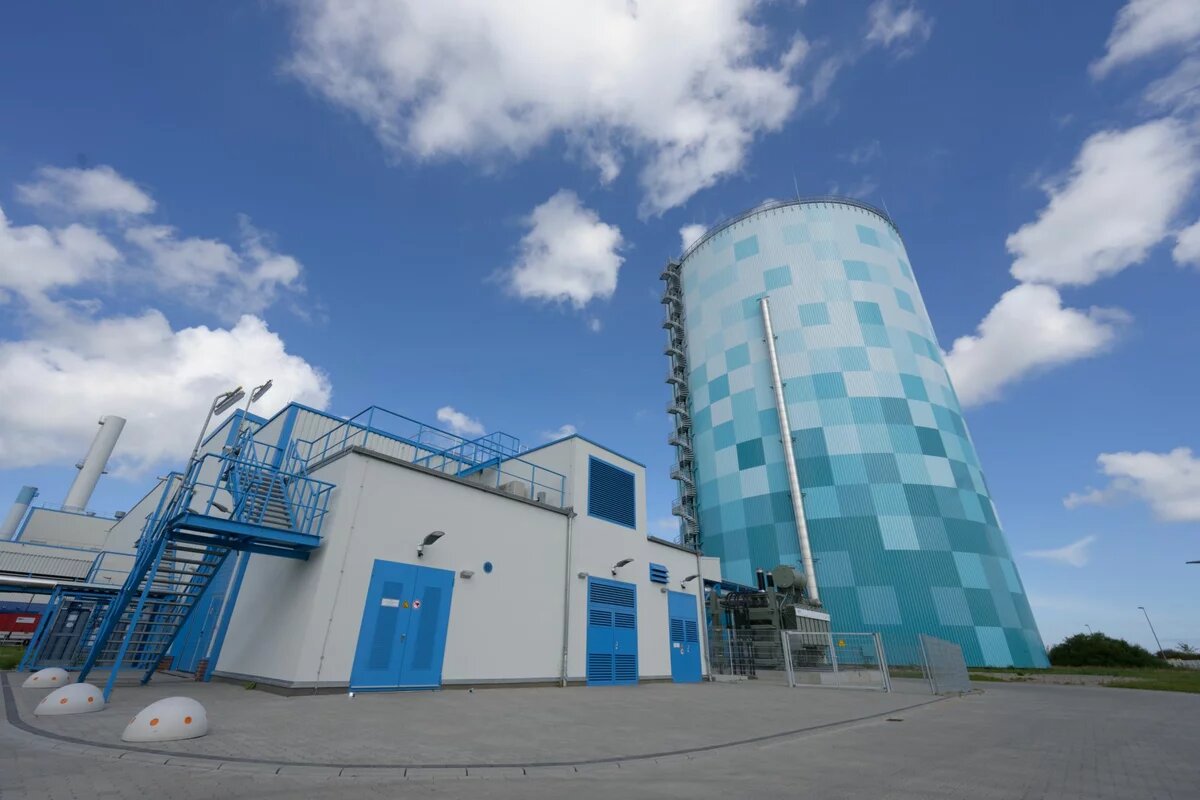 Dicker Blau-weiß karierter Turm neben einem einem weißem Technik-Gebäude mit blauen Türen und Treppen