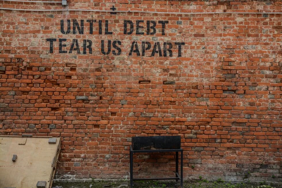 "Until Debt Tear us Apart" Eine Backsteinwand auf der in schwarzen Buchstaben steht: "Until Debt Tear us Apart"