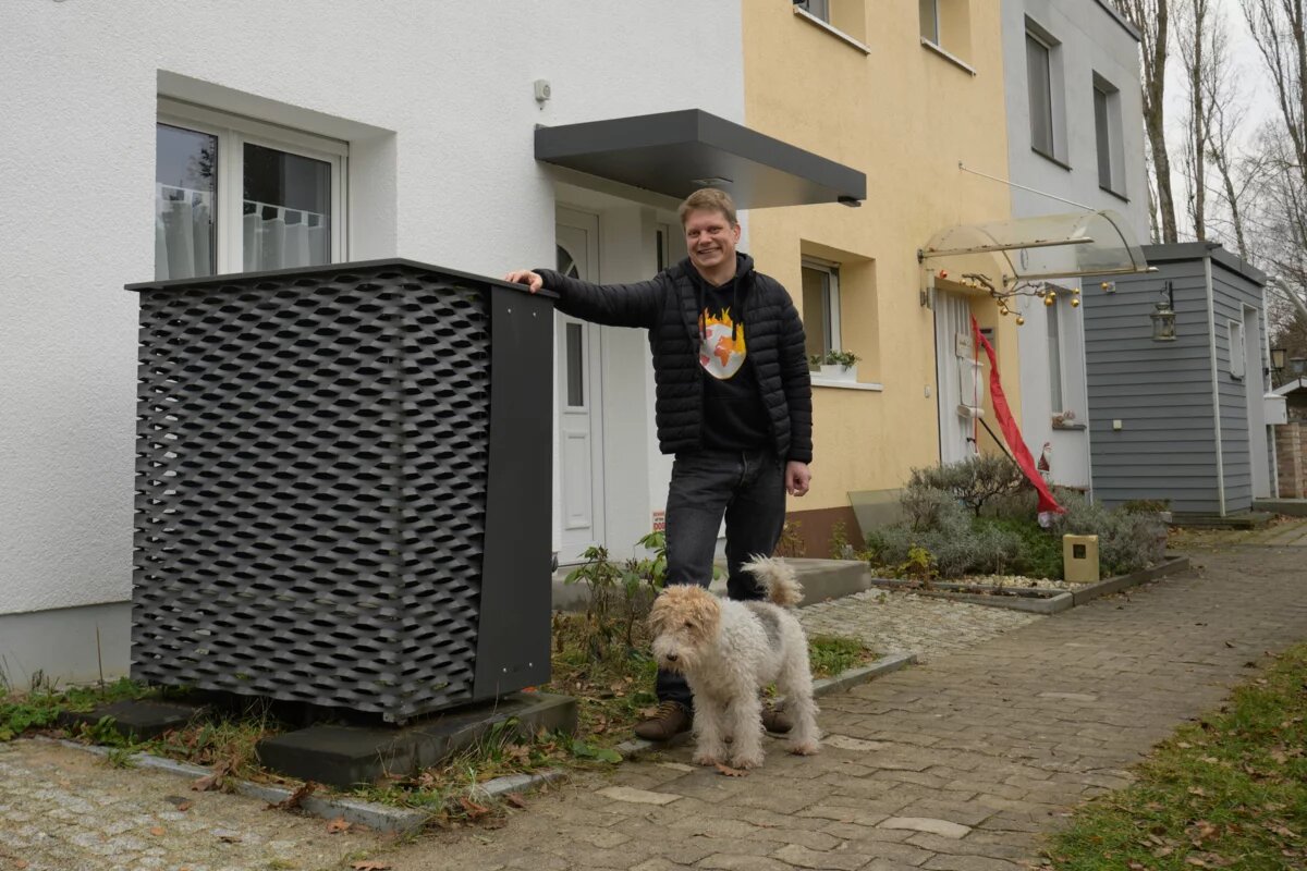 Tobias Zeller steht mit dem Familienhund vor seinem Einfamilienhaus und stützt sich an der Luft-Wasser-Wärmepumpe ab.