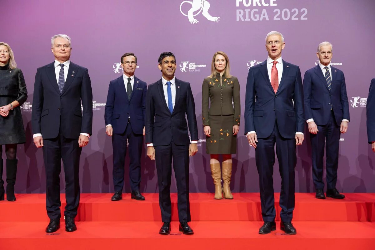 Excerpt from a group photo: Two women and six men stand together on a red staircase in front of a purple wall