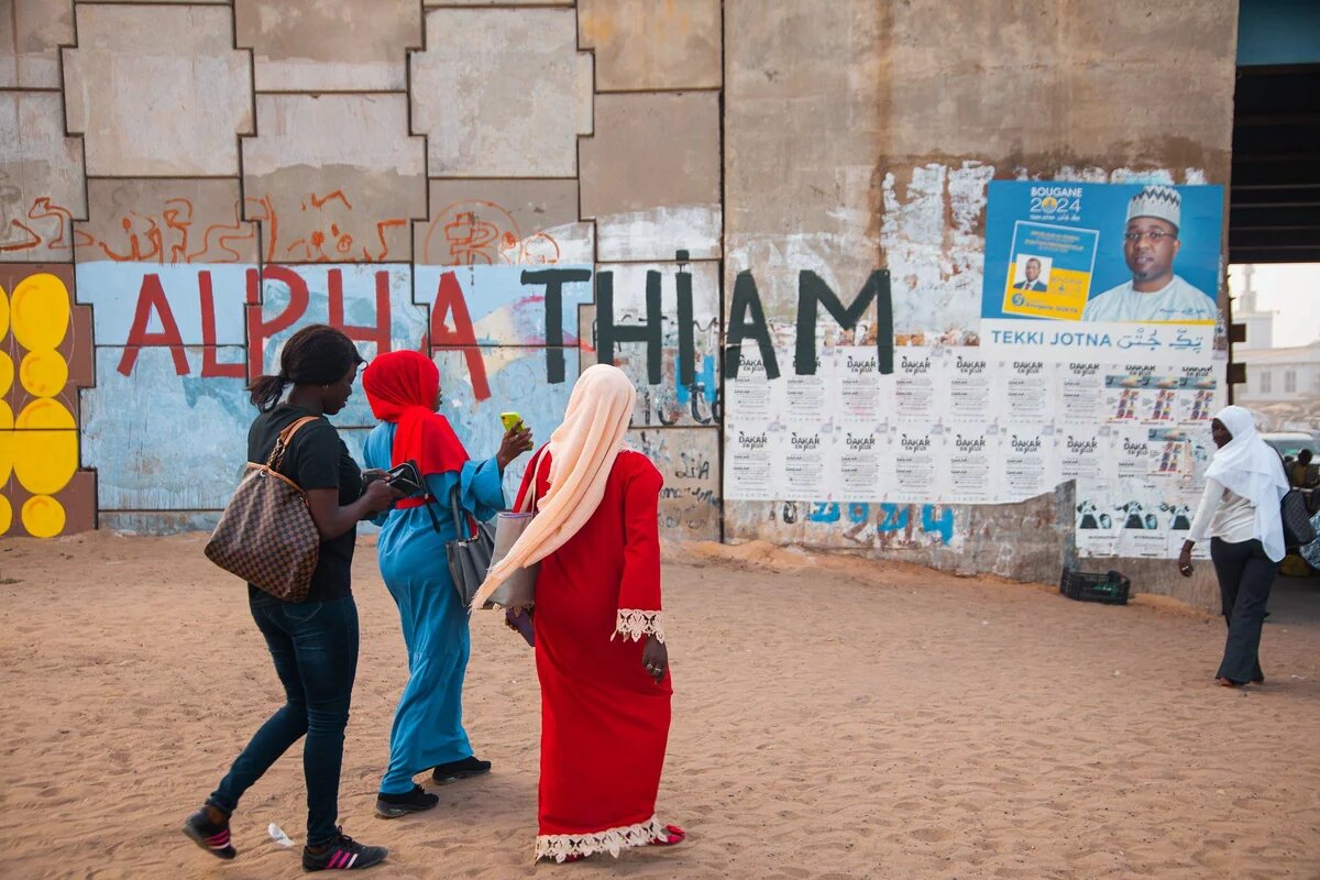 Drei Frauen laufen vor einer Wand mitr Wahplakaten lang. 