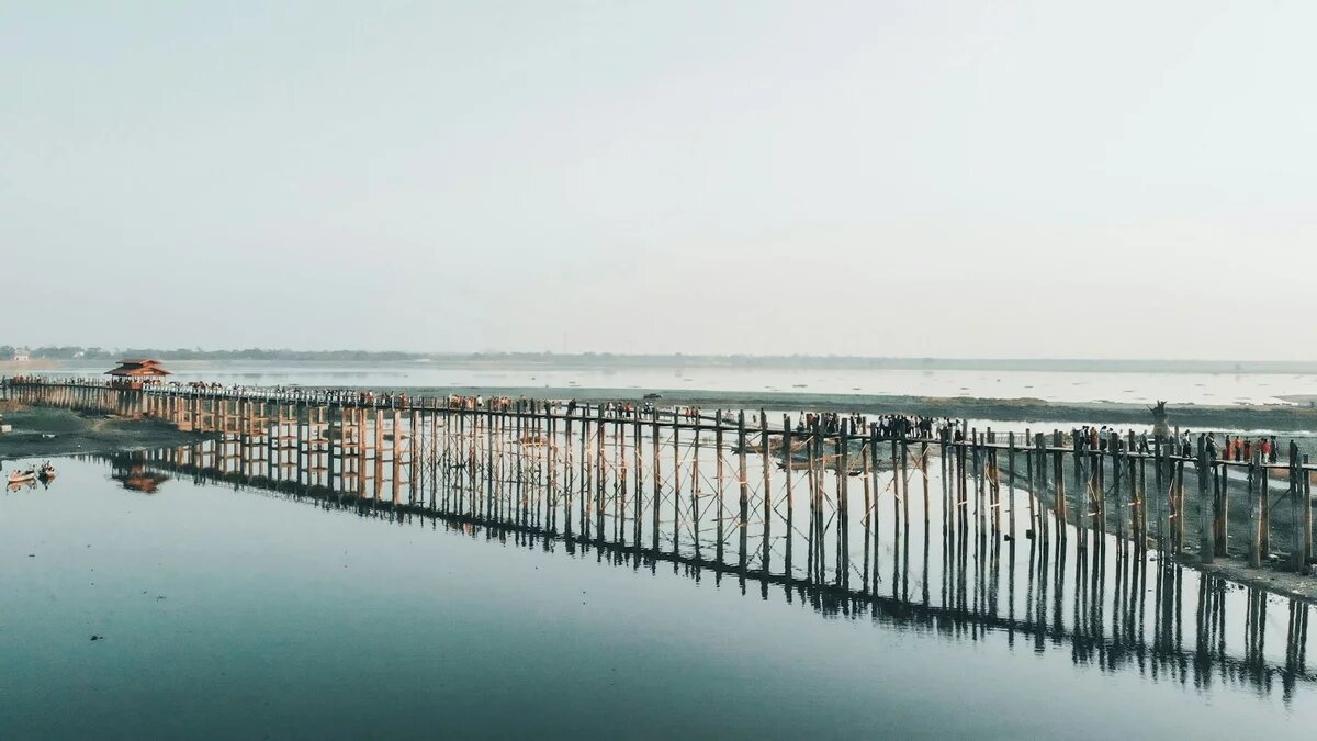 A footbridge runs on high, wooden stilts over a lake, with people walking across it.