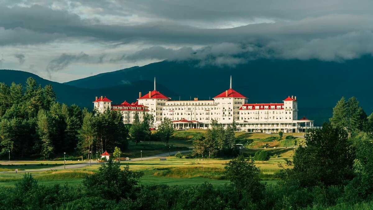 A white building with a red roof with mountains in the background