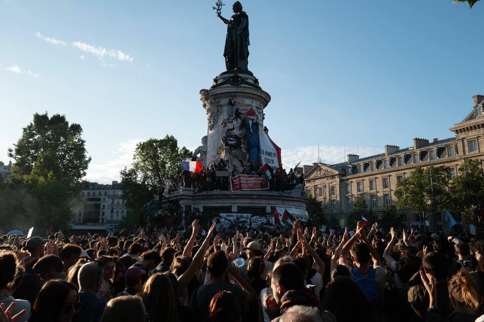 Foto: Paris, Place de la République. Eine Menschenmenge feiert nach der Wahl am 7. Juli 2024. Einige halten Fahnen und Transparente.