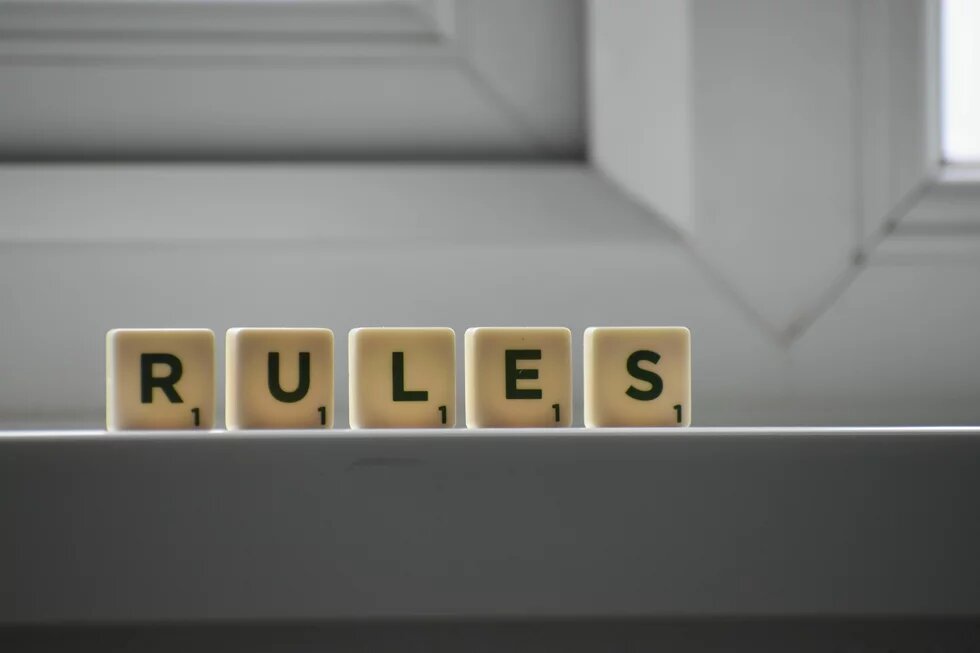 Rules (Regeln) Fünf Spielsteinwürfel mit dem Wort „RULES“ (Regeln) stehen auf einer Fensterbank.