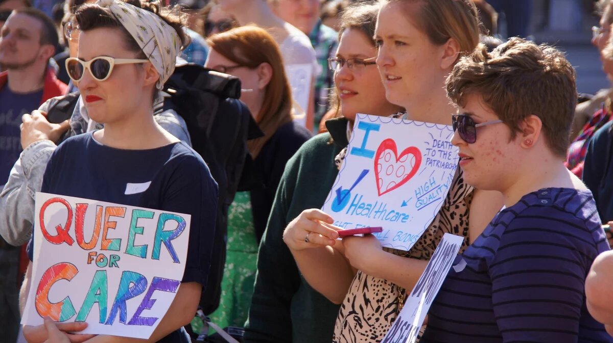 People on a rally for transgender equality, sign saying "queer for care"